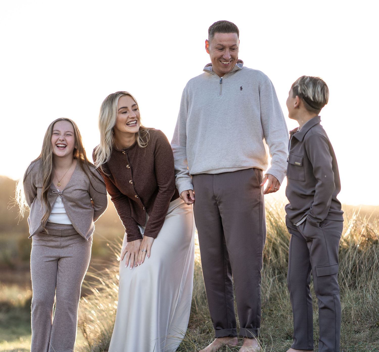 Family laughs together during golden hour photoshoot in a field of tall grass at sunset.