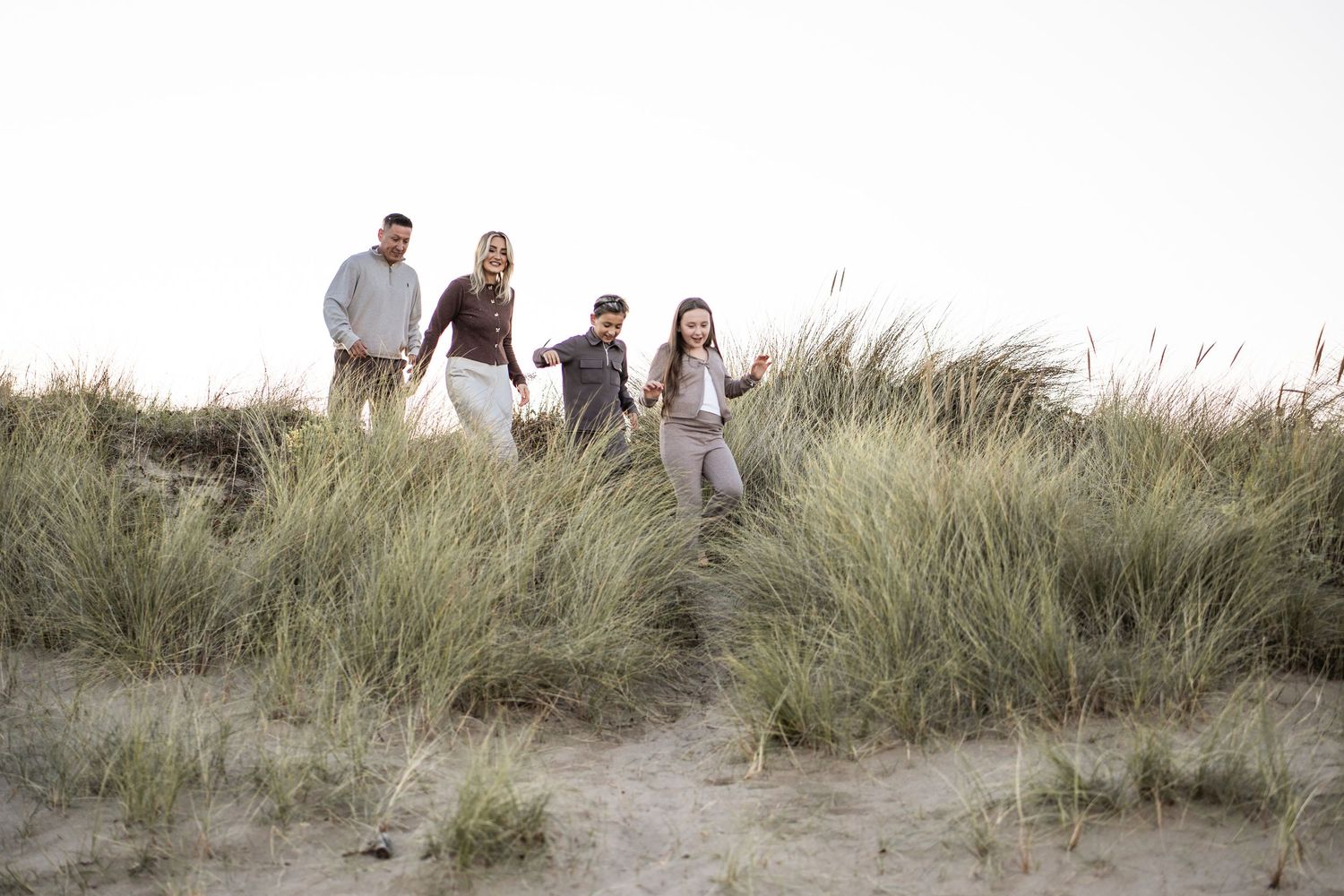 A group walks together along grassy sand dunes at the beach during sunset.