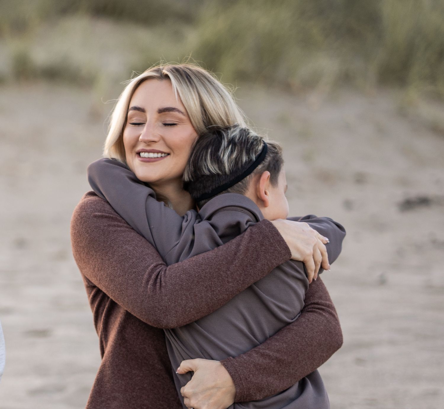 Two people share a warm embrace on a sandy beach during an emotional moment.