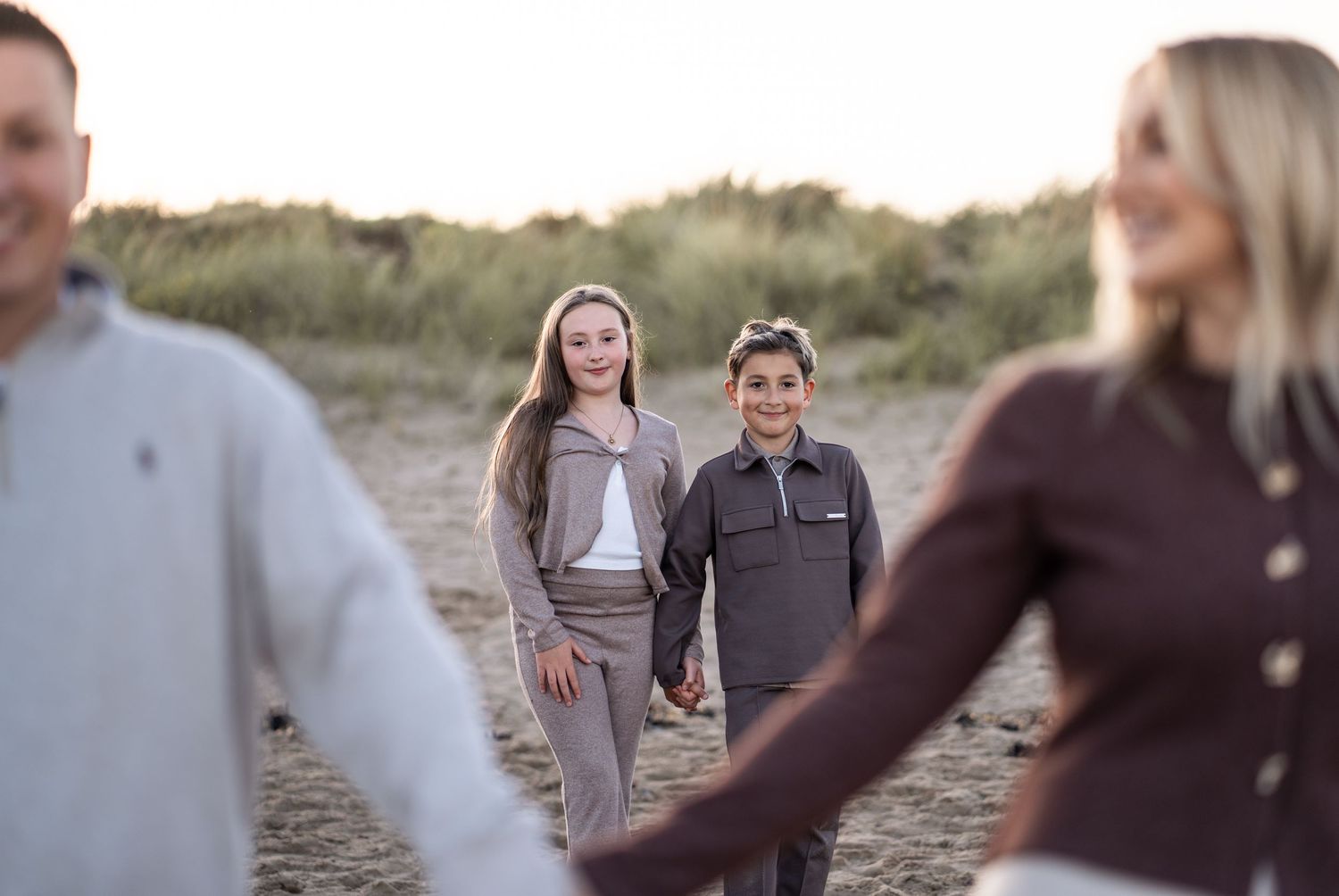 A group walks together on a sandy path through coastal dunes during golden hour.