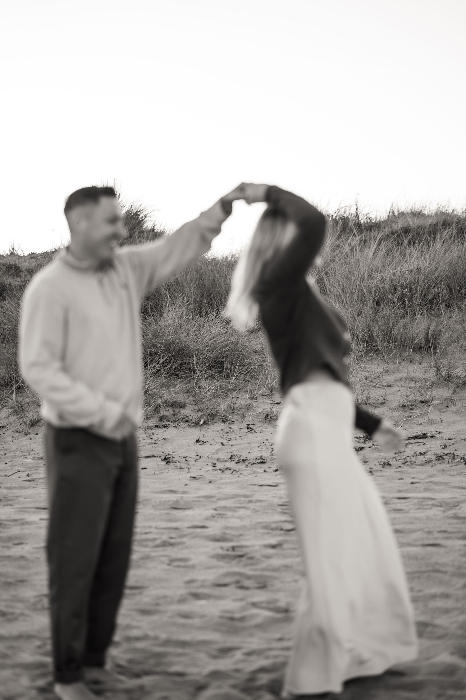 A series of black and white photos showing a couple dancing playfully on a beach.