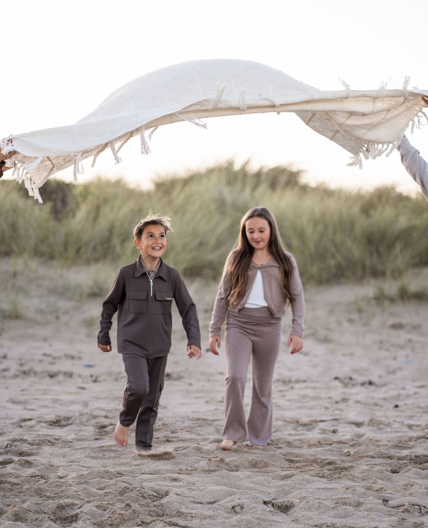 People walking and playing together on a sandy beach with dunes in the background.