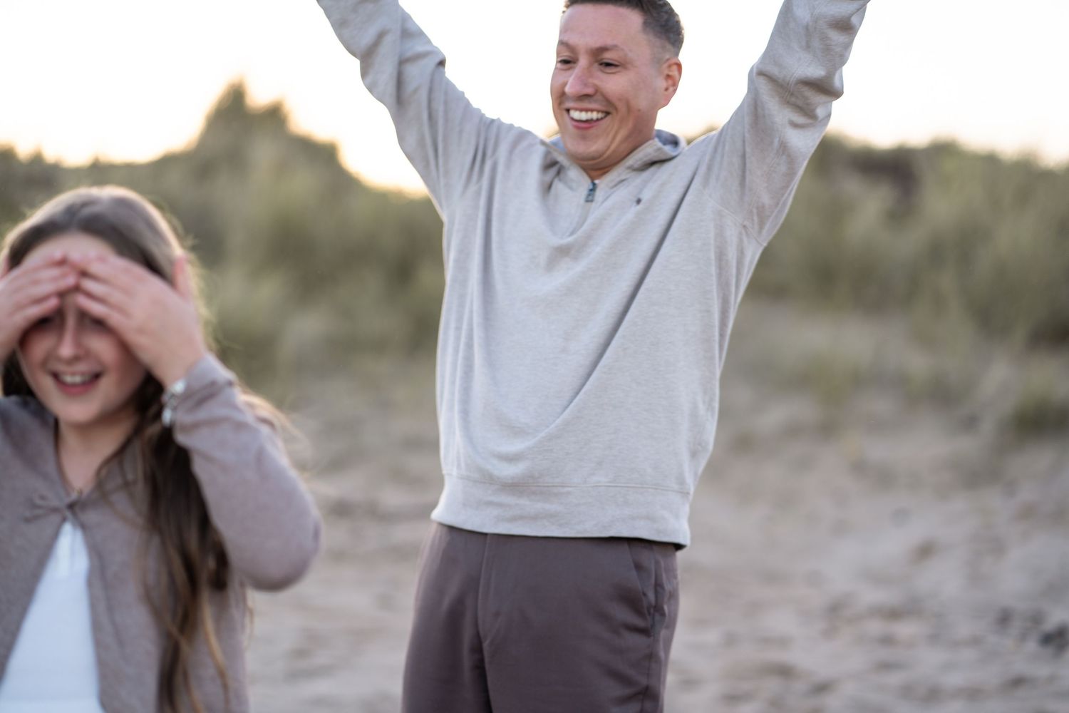 A group of people wearing light colored shirts laugh and smile together outdoors in a natural setting at sunset.
