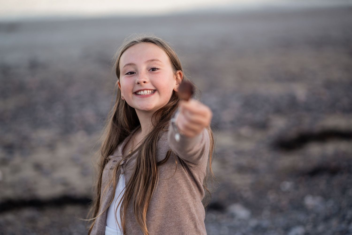 Child with long hair playing and smiling on a rocky beach.