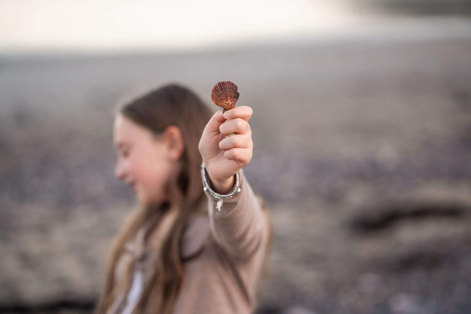 Child holding up a small object while playing on a beach at sunset.