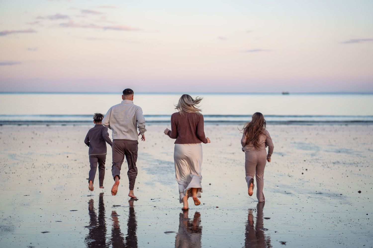 Family walking together along a serene beach shoreline at sunset with reflections in the wet sand.