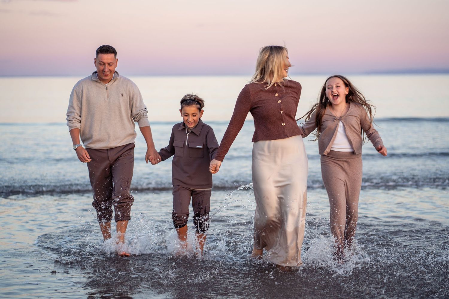 Group enjoying a beach walk while splashing in the surf during golden hour.