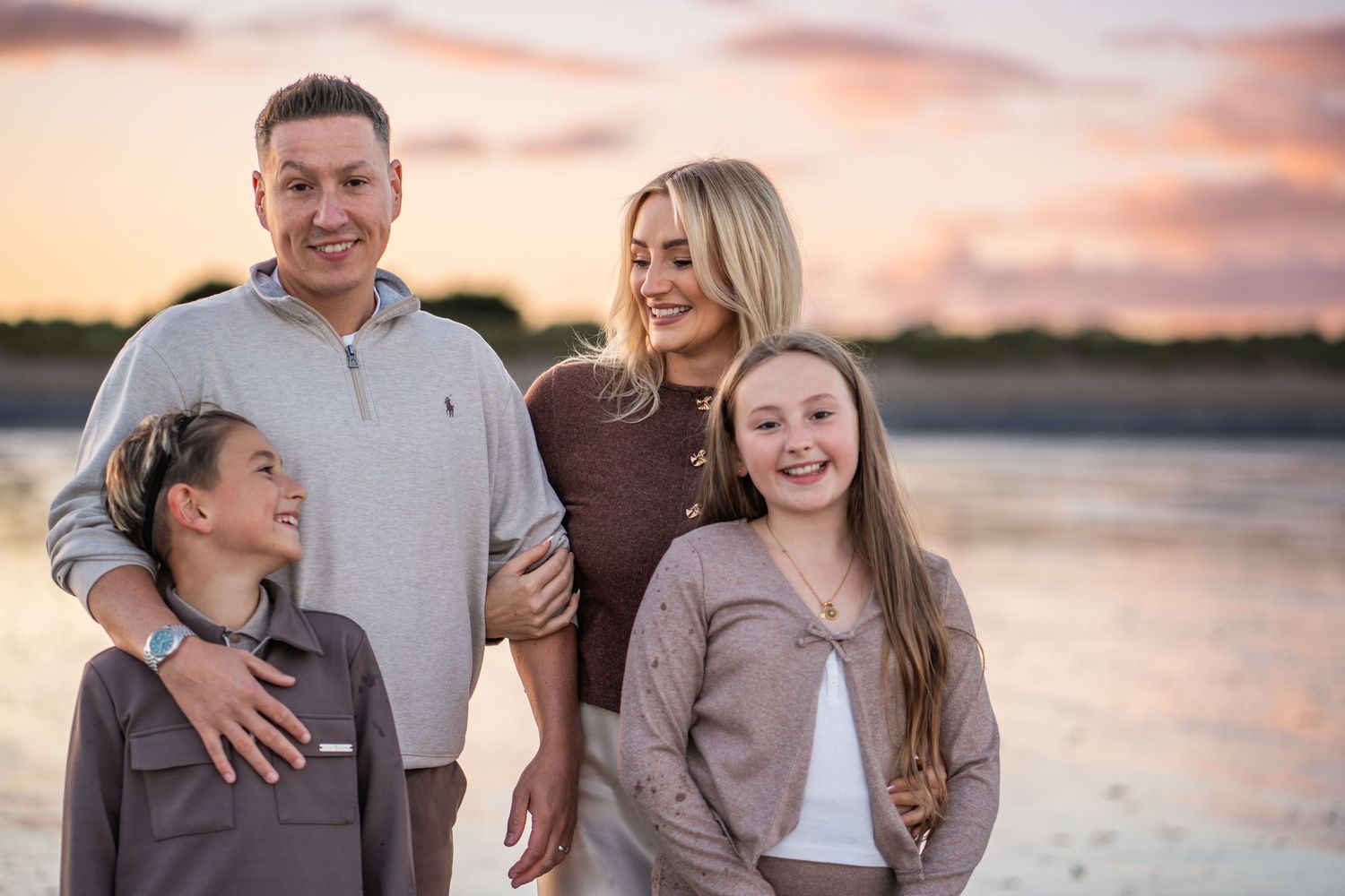 Family group enjoying a sunset photoshoot by the water in coordinated neutral outfits.