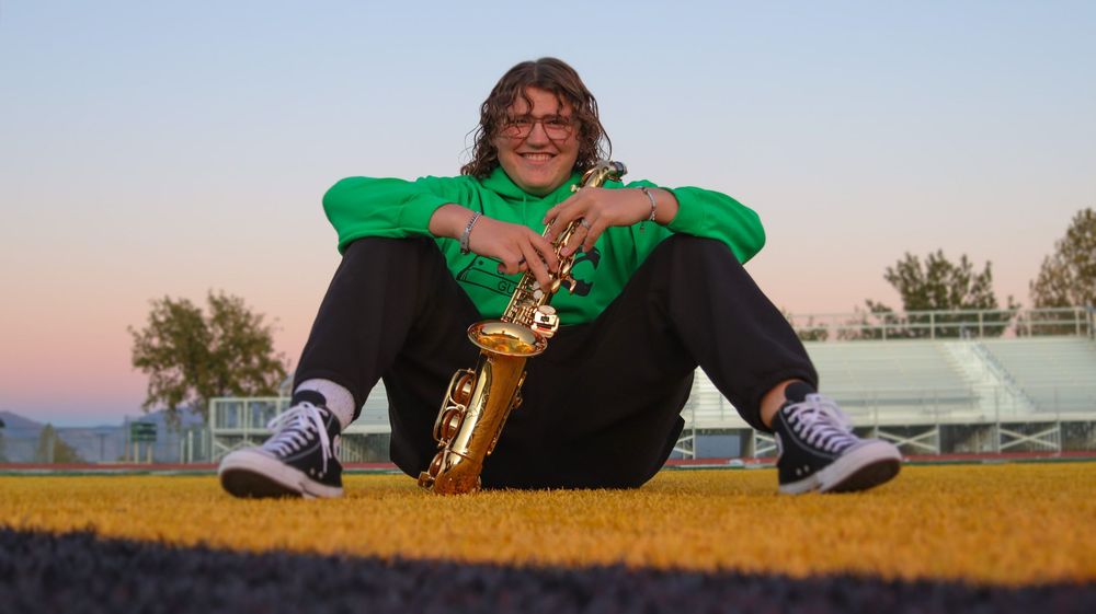 Teen boy sitting on a field with a saxophone during a candid senior photo session in Utah