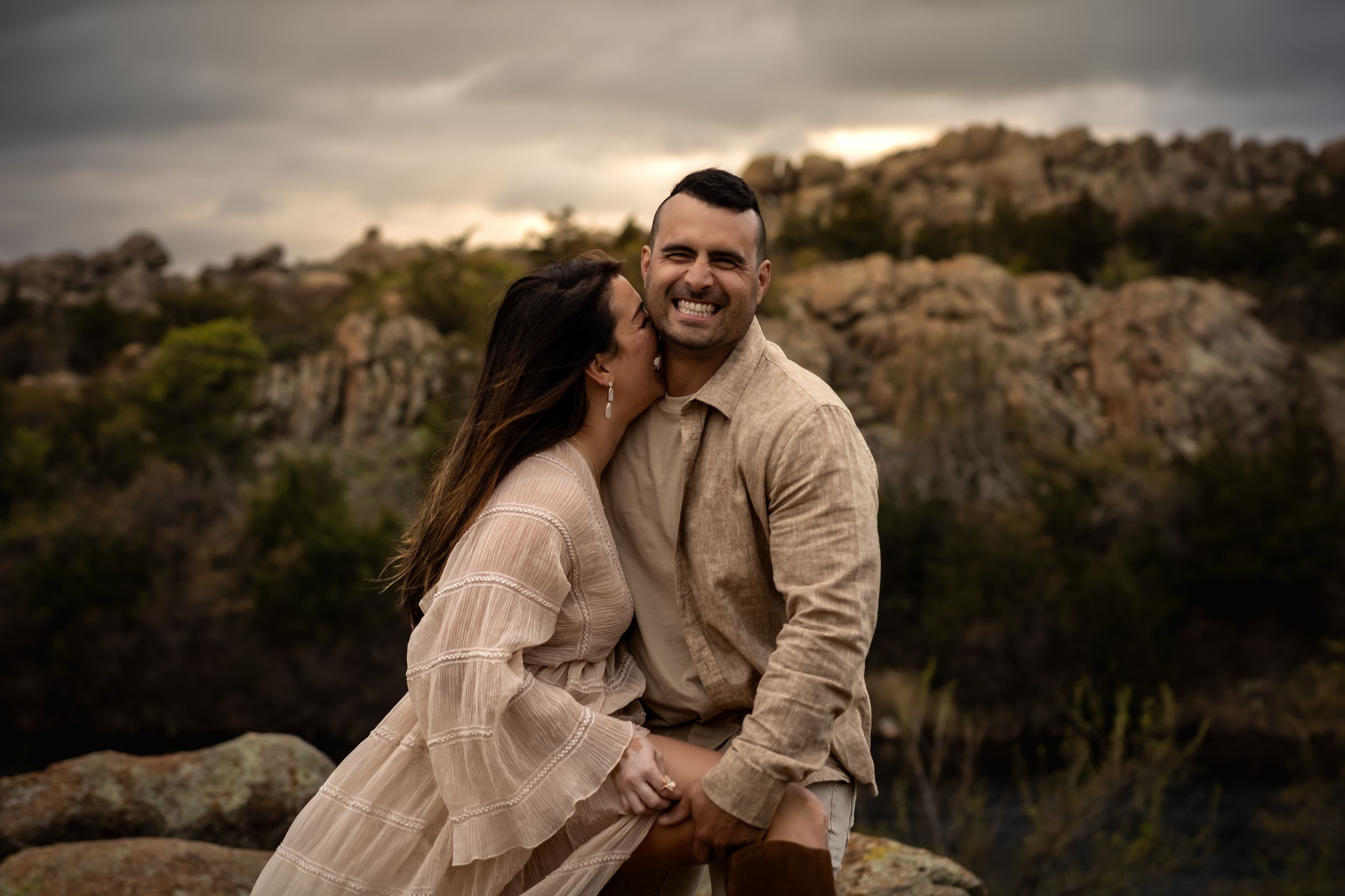 Romantic mountain photoshoot with couple in flowing dress against rocky landscape.