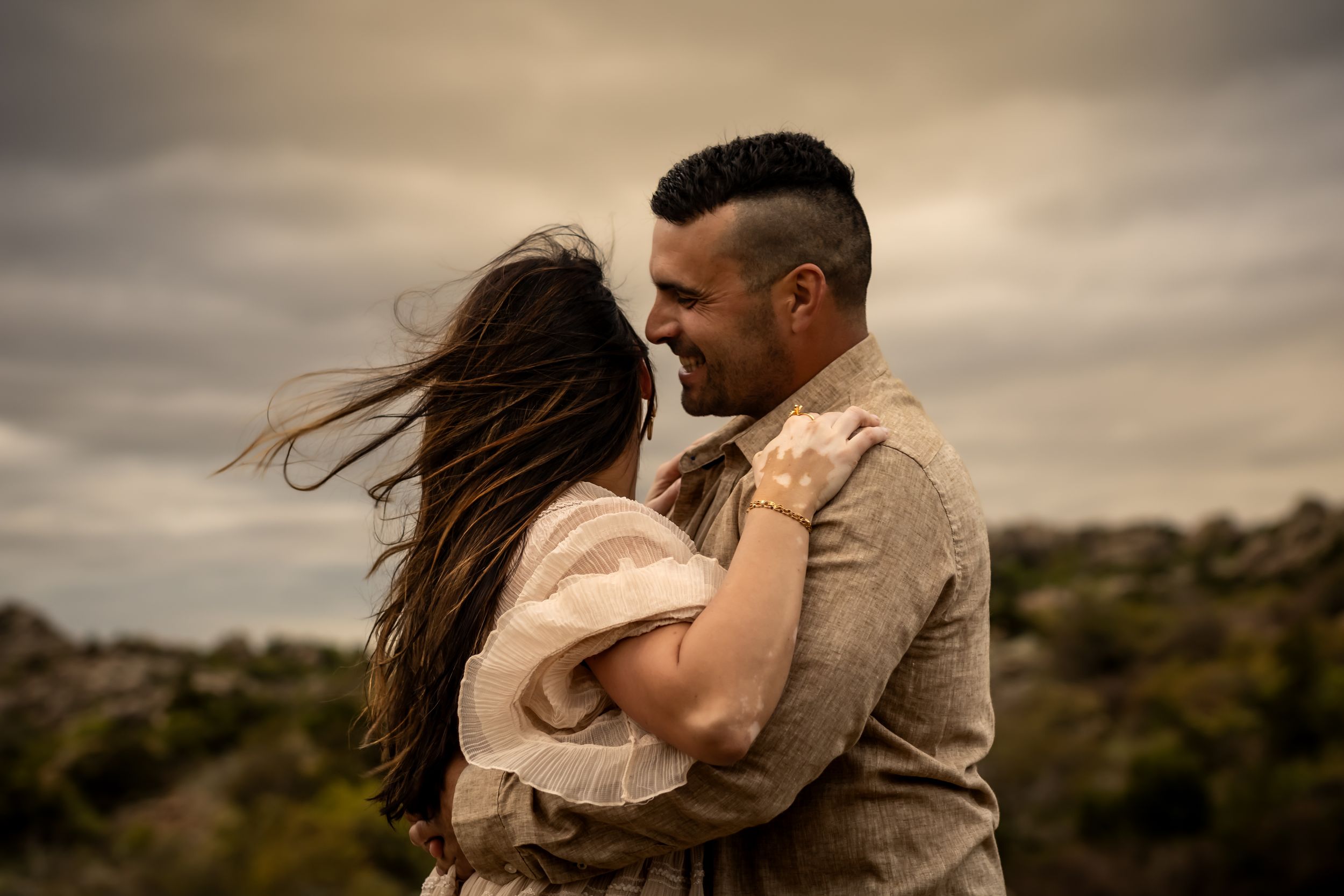 Couple embraces passionately against dramatic cloudy sky at sunset.