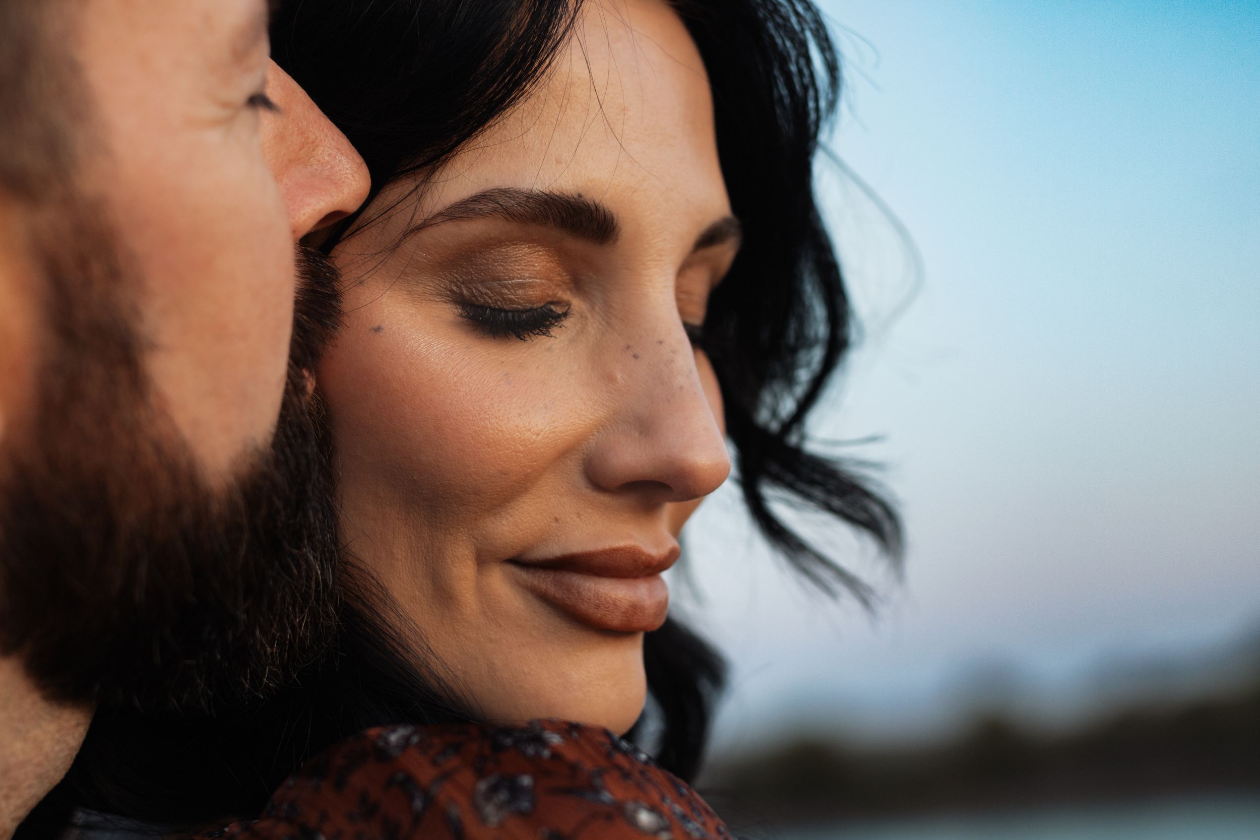 Close-up portrait capturing intimate moment against blue sky background.