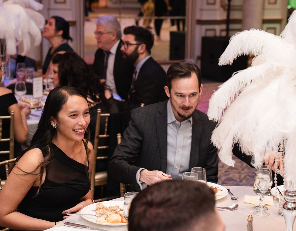 Guests enjoy an elegant dinner party with white feather centerpieces and formal table settings at an upscale venue.