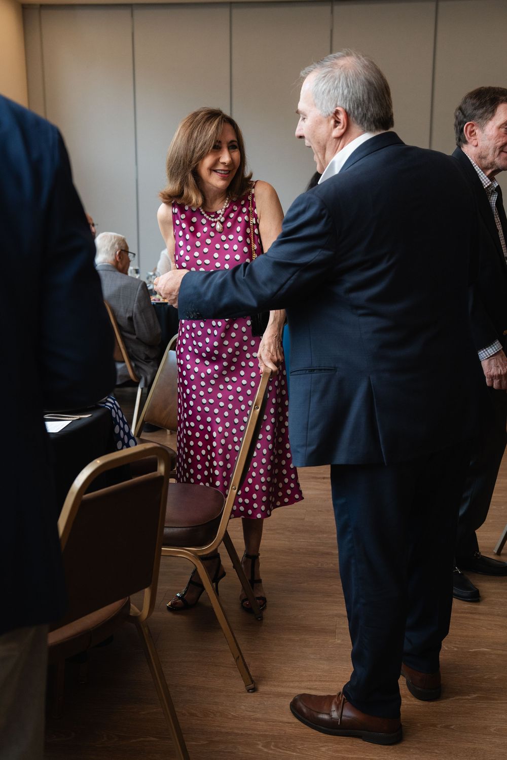 Woman in polka dot dress shaking hands with man in navy suit at formal networking event.