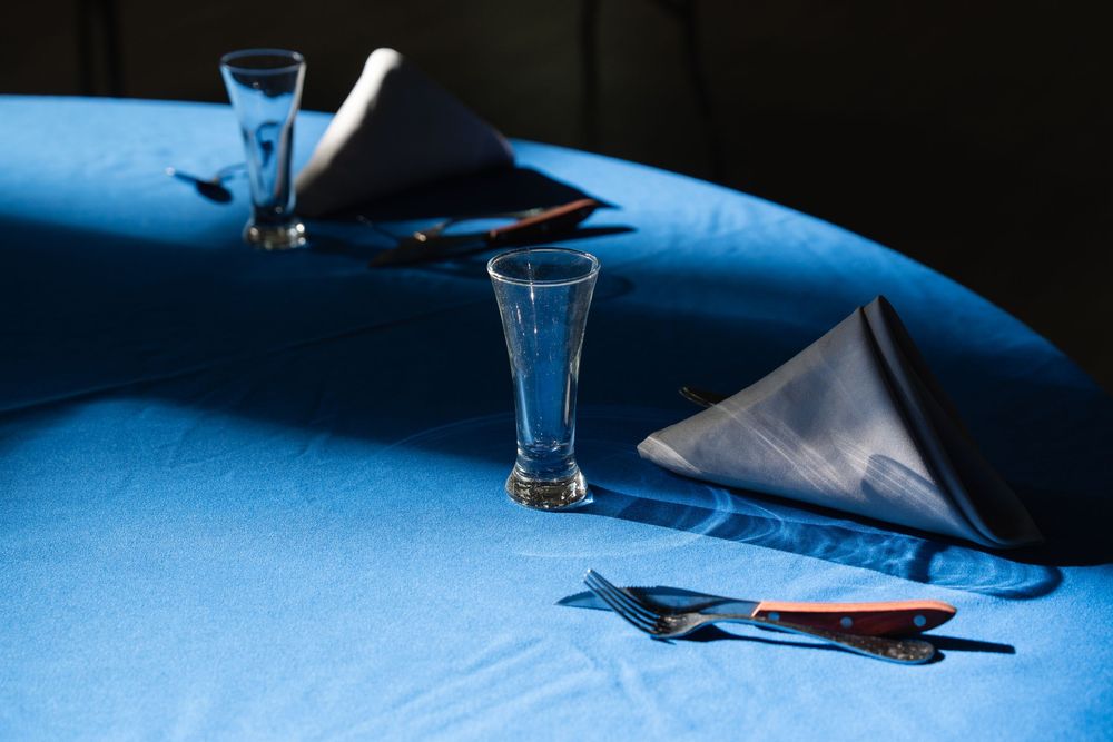 Blue tablecloth set with glass vases, gray folded napkins, and cutlery in an elegant restaurant table setting.