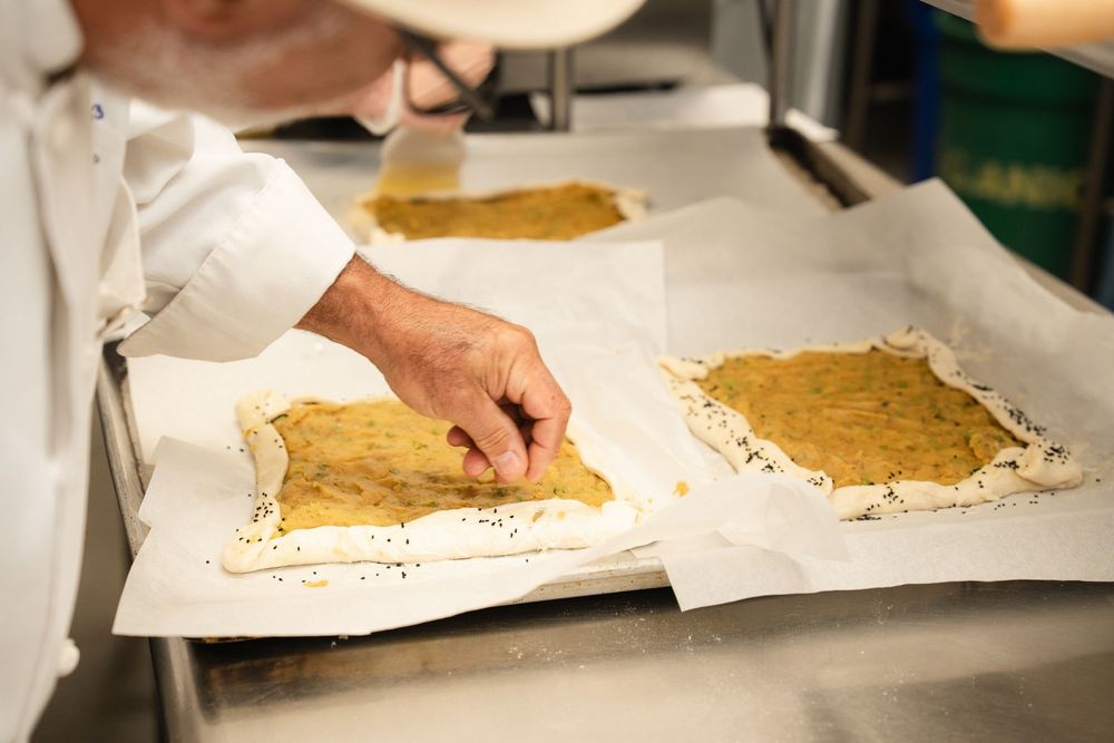 Baker placing filling onto dough sheets on parchment-lined baking trays in a professional kitchen.