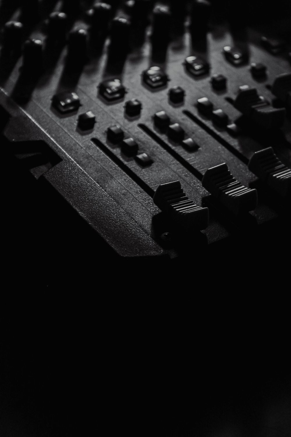 Close-up black and white photo of a professional audio mixing console with faders and knobs.