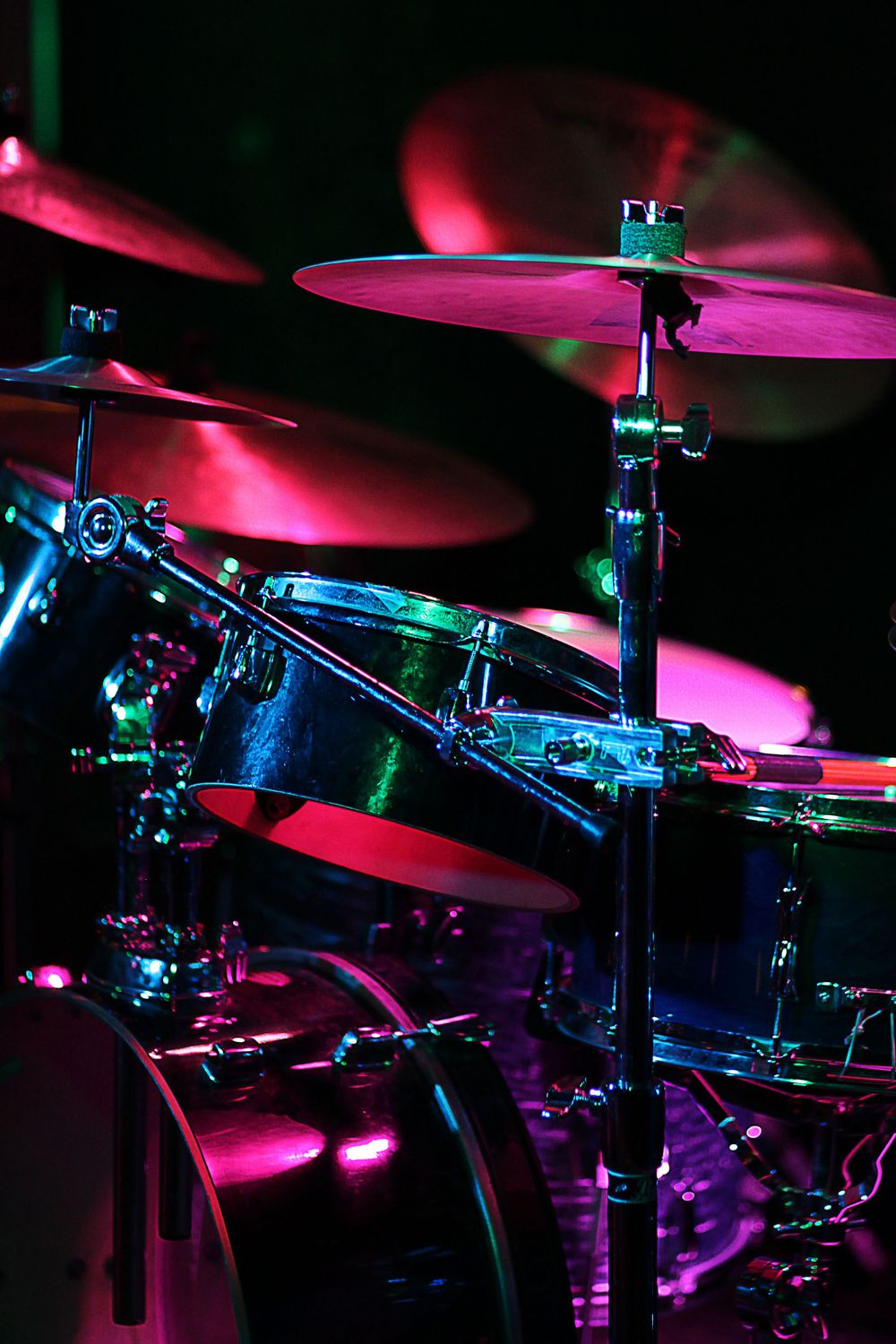 Colorful drum kit illuminated by pink and teal stage lights during a live music performance.