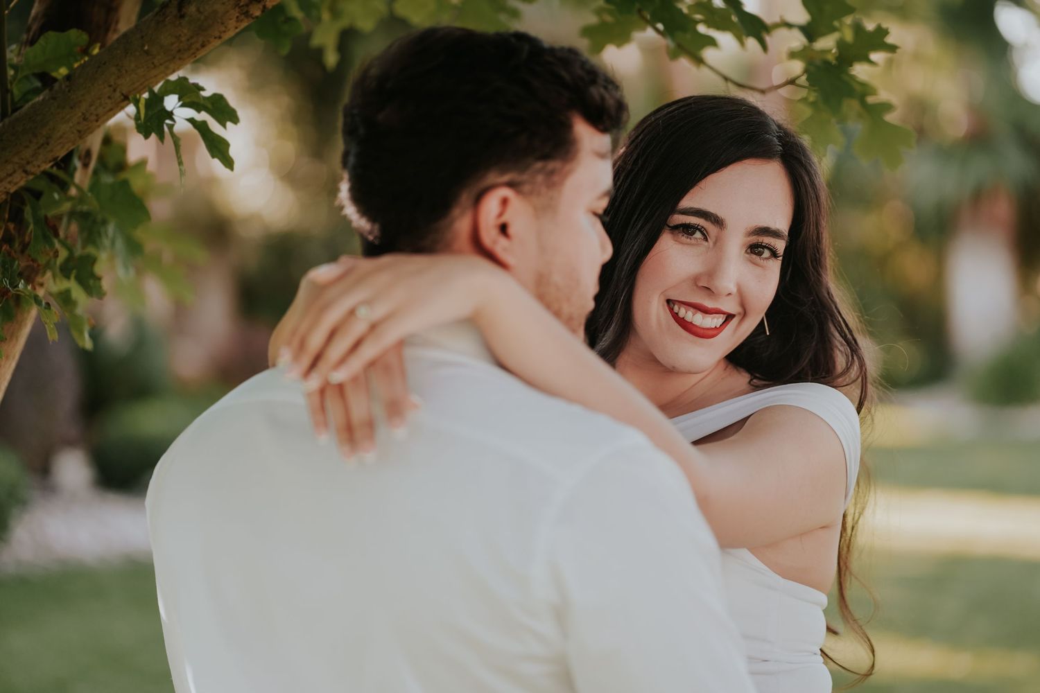 A couple embraces during an outdoor wedding photoshoot in a sunlit garden setting.