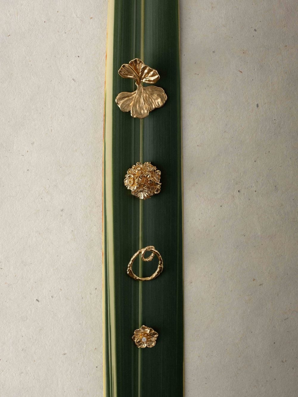Gold butterfly-shaped jewelry pieces arranged on a dark green leaf against a white background.