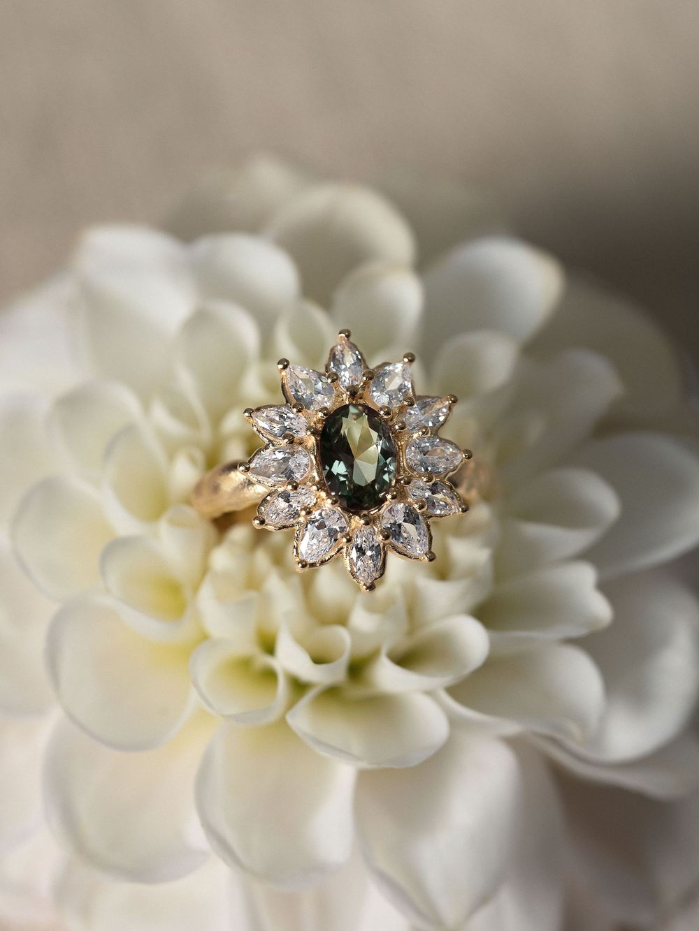 Elegant diamond cluster ring with emerald center stone displayed on delicate white dahlia flower petals.