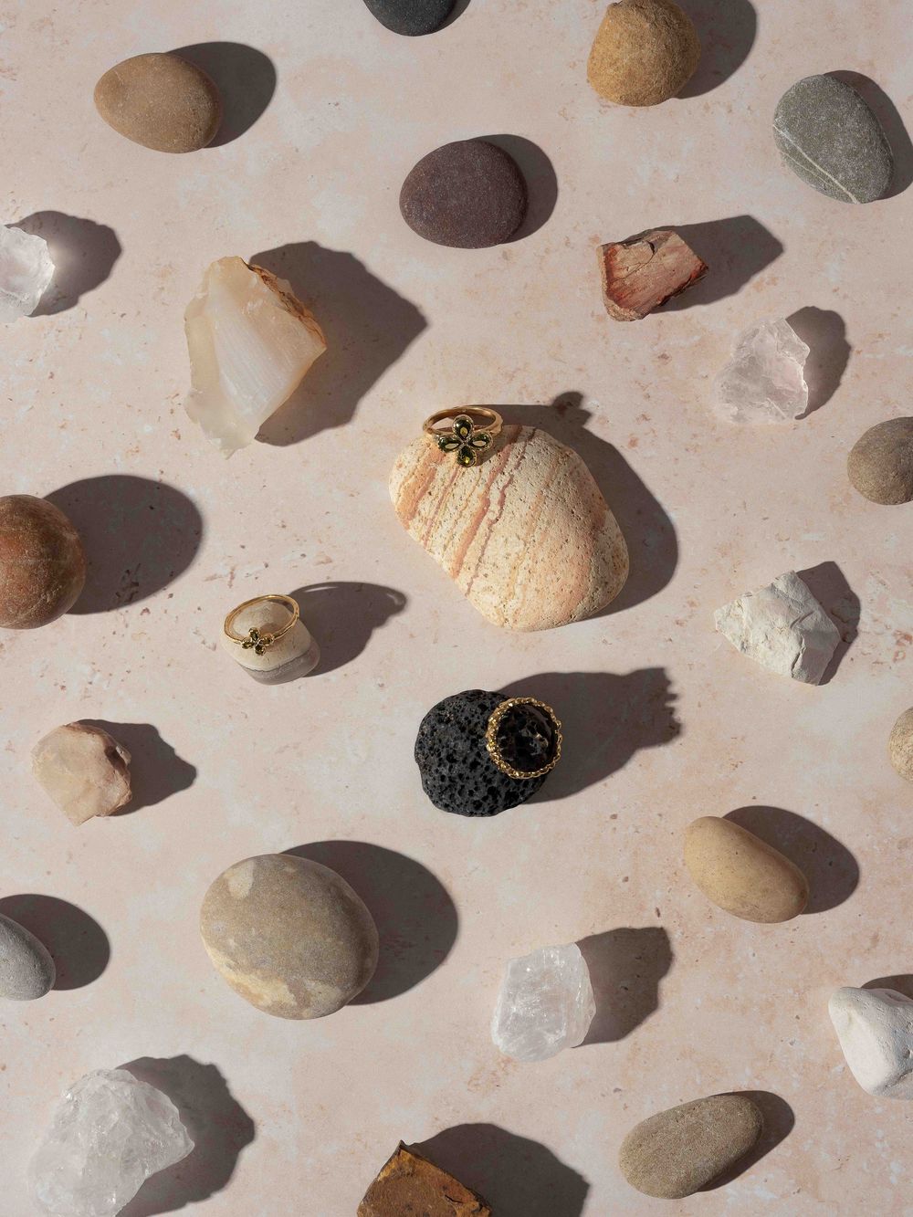 Collection of small pebbles and stones arranged on a light beige surface casting soft shadows.