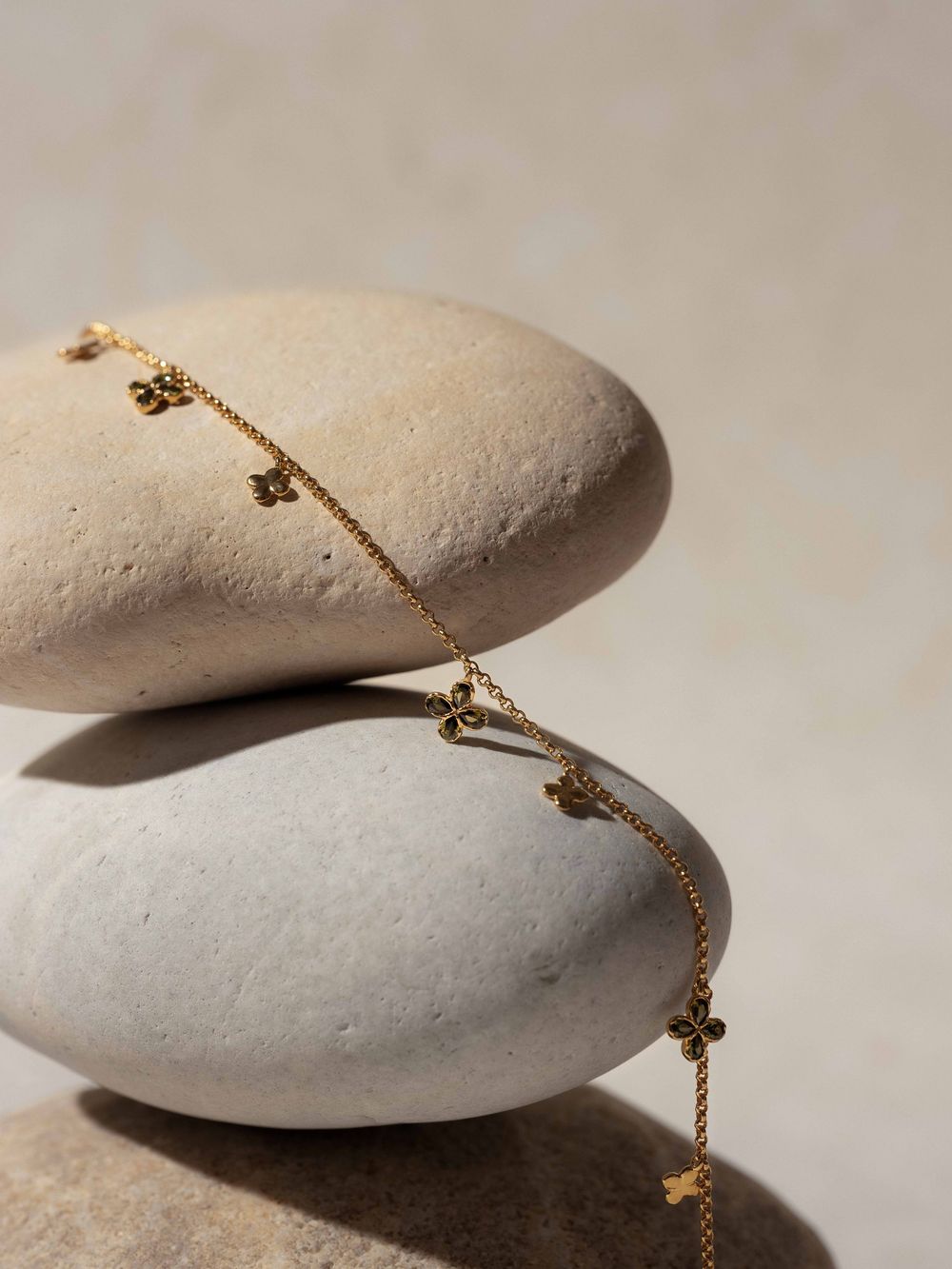 Delicate gold chain bracelet with tiny charms draped across smooth white stones in minimalist composition.
