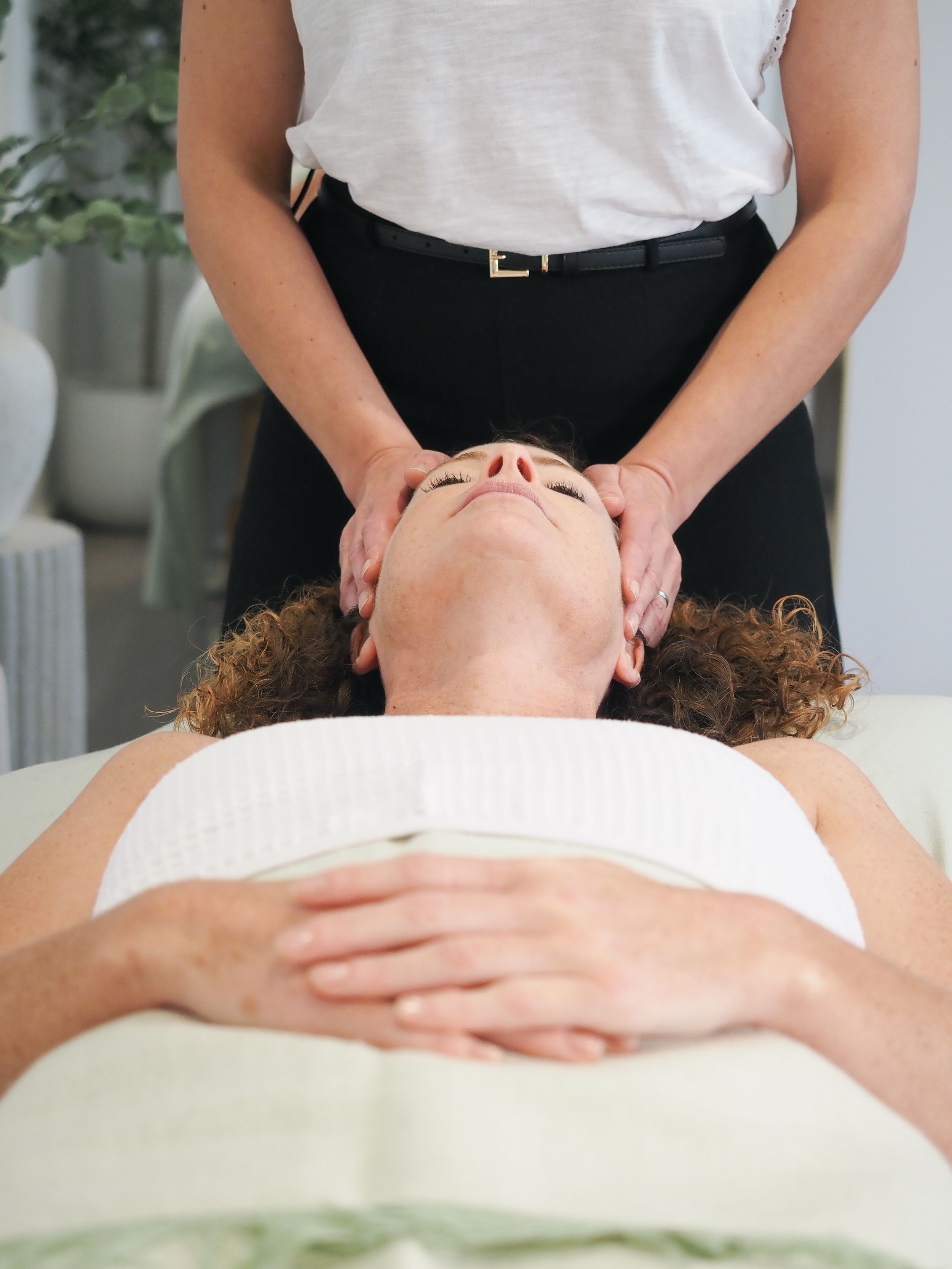 Therapeutic facial massage being performed on massage table with white linens in serene spa environment.
