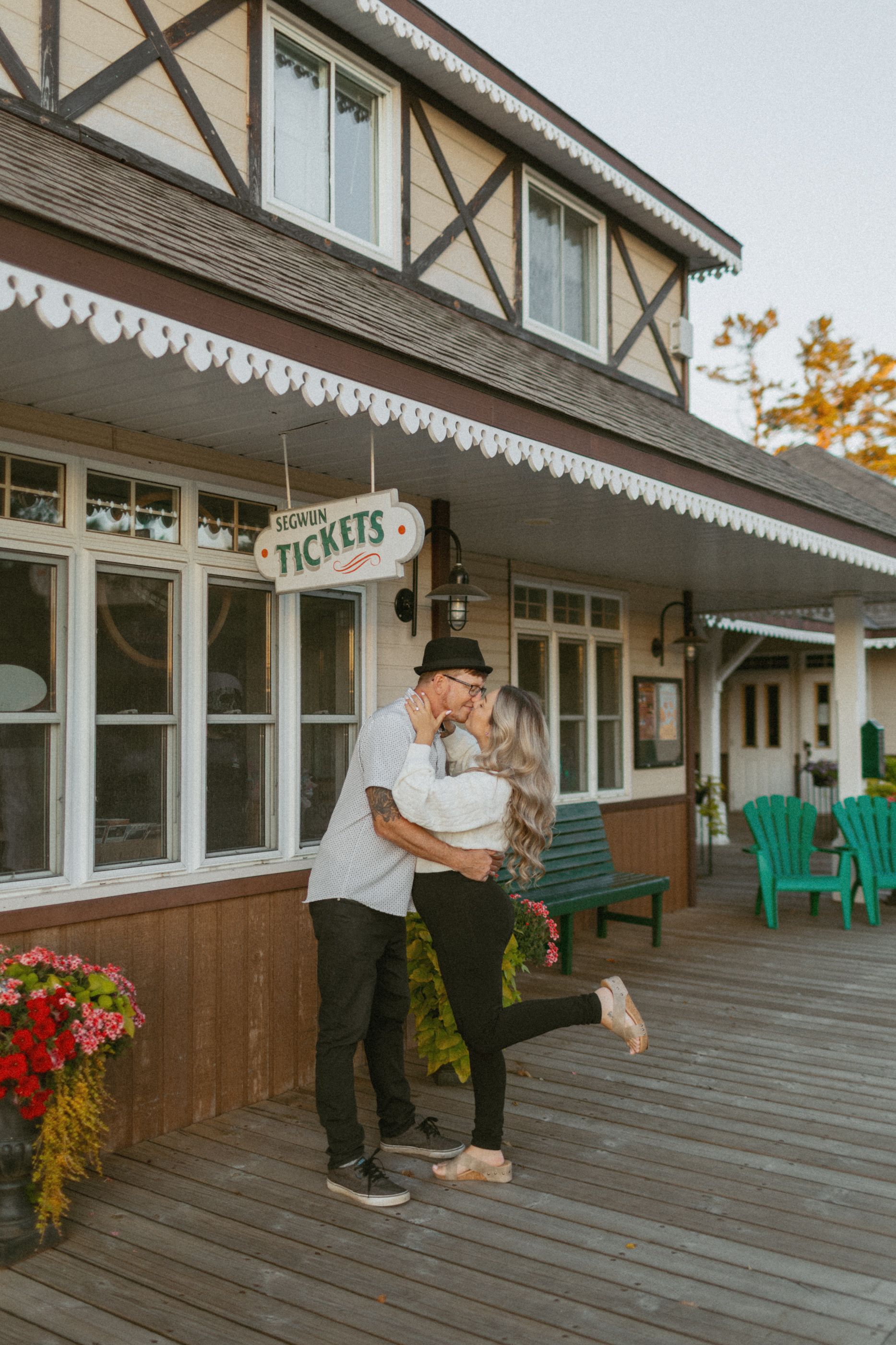 Couple sharing a romantic moment on a wooden deck with ticket booth in background.