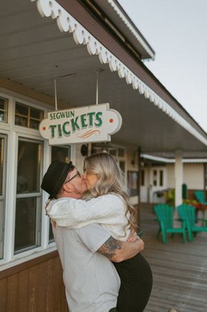 Romantic embrace on a wooden deck with vintage ticket booth signage.