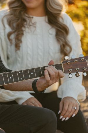 Close-up of hands holding an acoustic guitar wearing a white sweater.