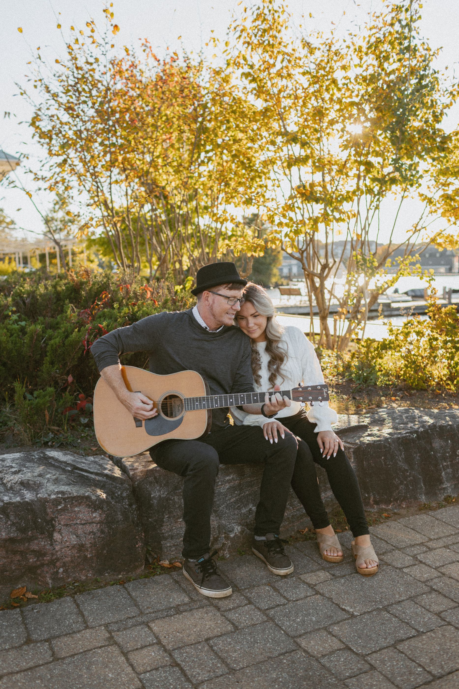 A couple relaxes on stone steps with an acoustic guitar during golden hour.