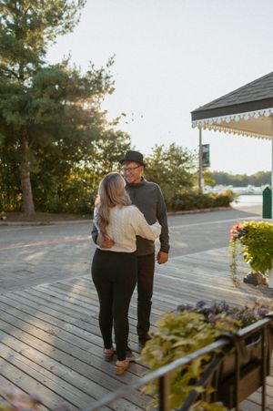 Two people embrace while walking on a wooden deck at sunset.