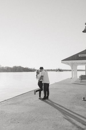 Black and white photo of two people casting long shadows on a waterfront path.