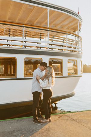 Couple standing beside a vintage riverboat at sunset.