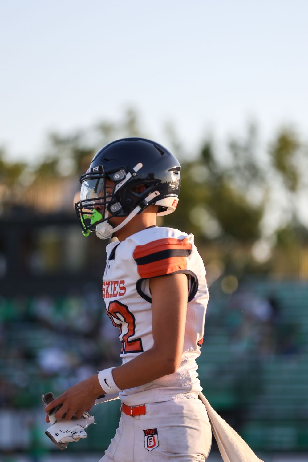 Football players in white uniforms with orange trim stand on field during a sunny afternoon game.