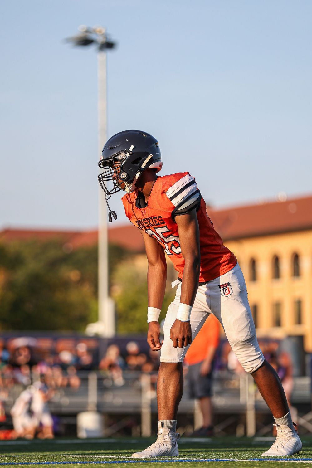Football players in orange jerseys line up in three-point stances on the field.