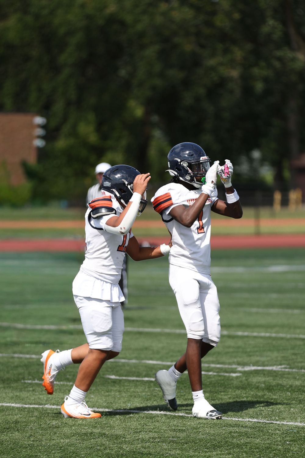 Football players in white uniforms practice stretching exercises on a grass field during training.