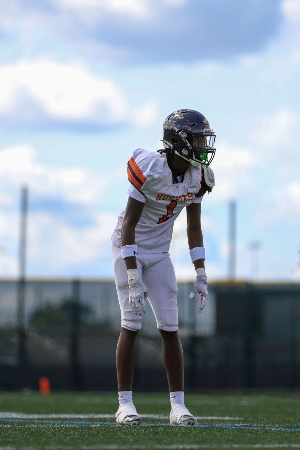 Football player in white uniform crouches in ready position on field during game preparation.