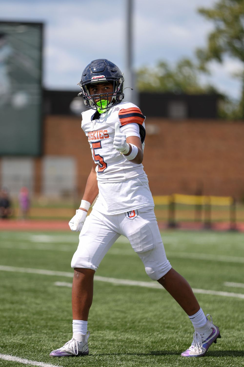Football player in white uniform demonstrates defensive stance on grass field during practice session.