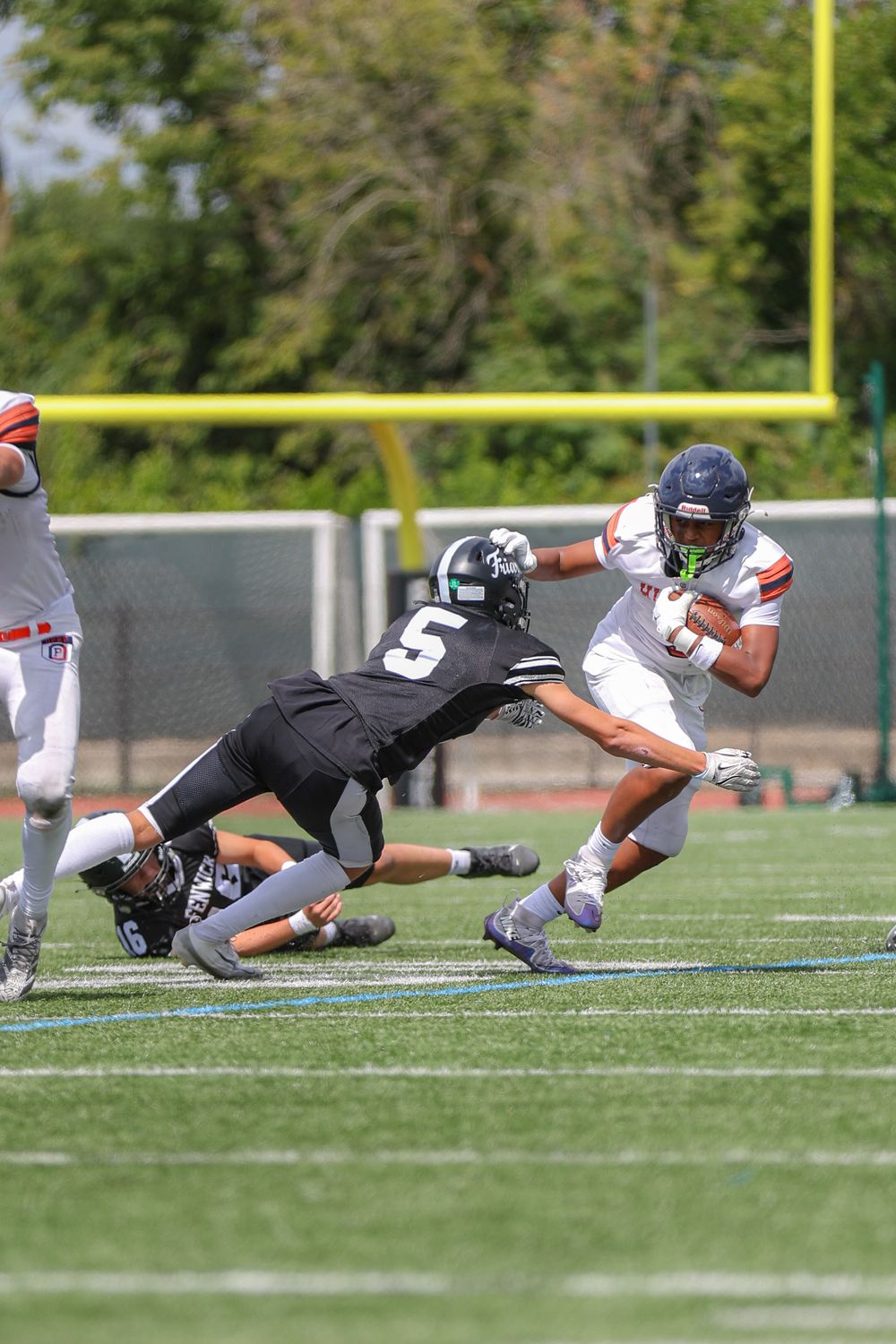 Football player in white jersey evades tackle attempt from defender in black uniform during game on turf field.