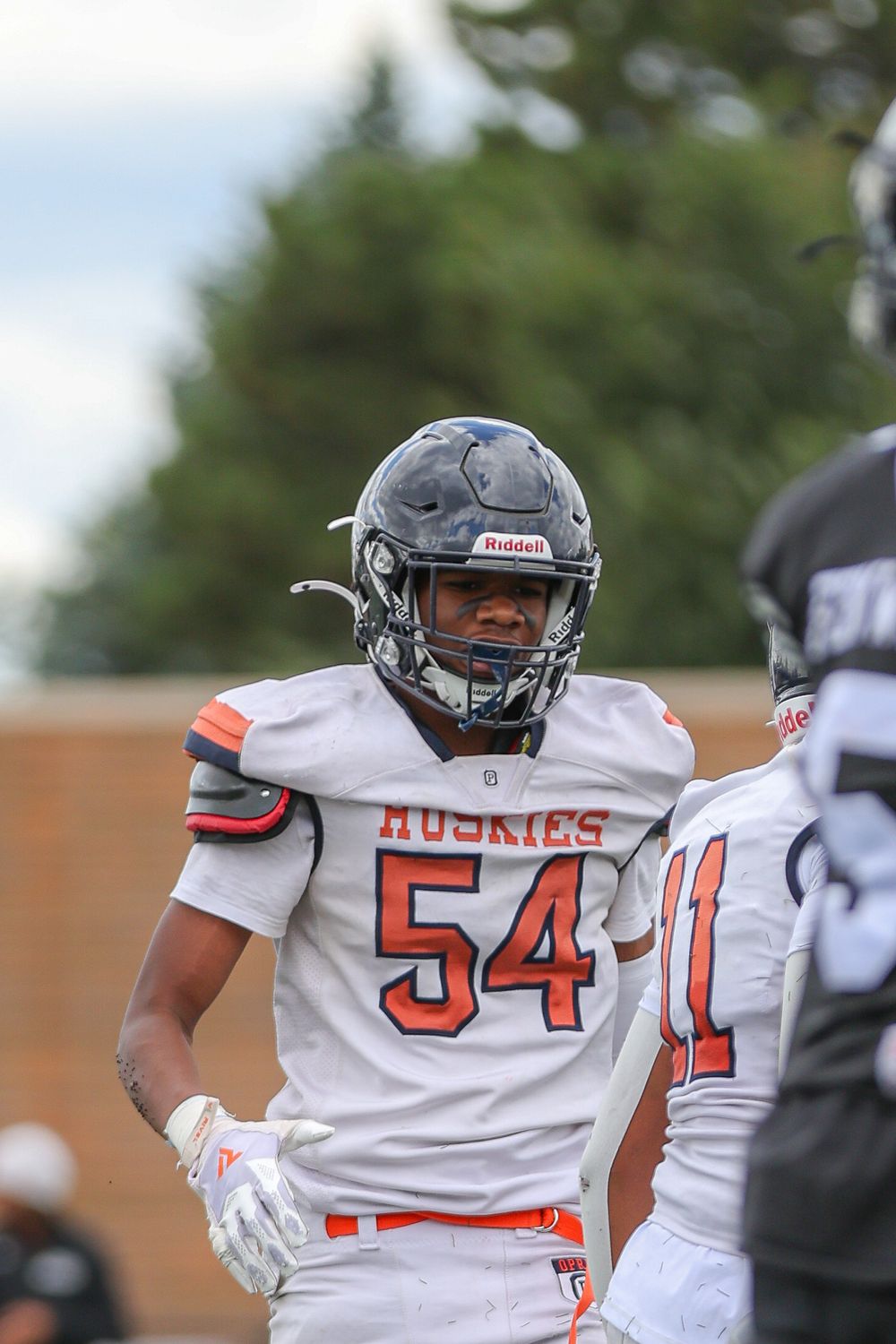 Football players in white uniforms with orange numbers and black helmets line up during a game.