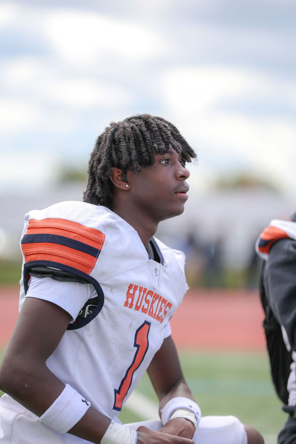 Football players in white jerseys with orange accents stand on the sidelines during a game.