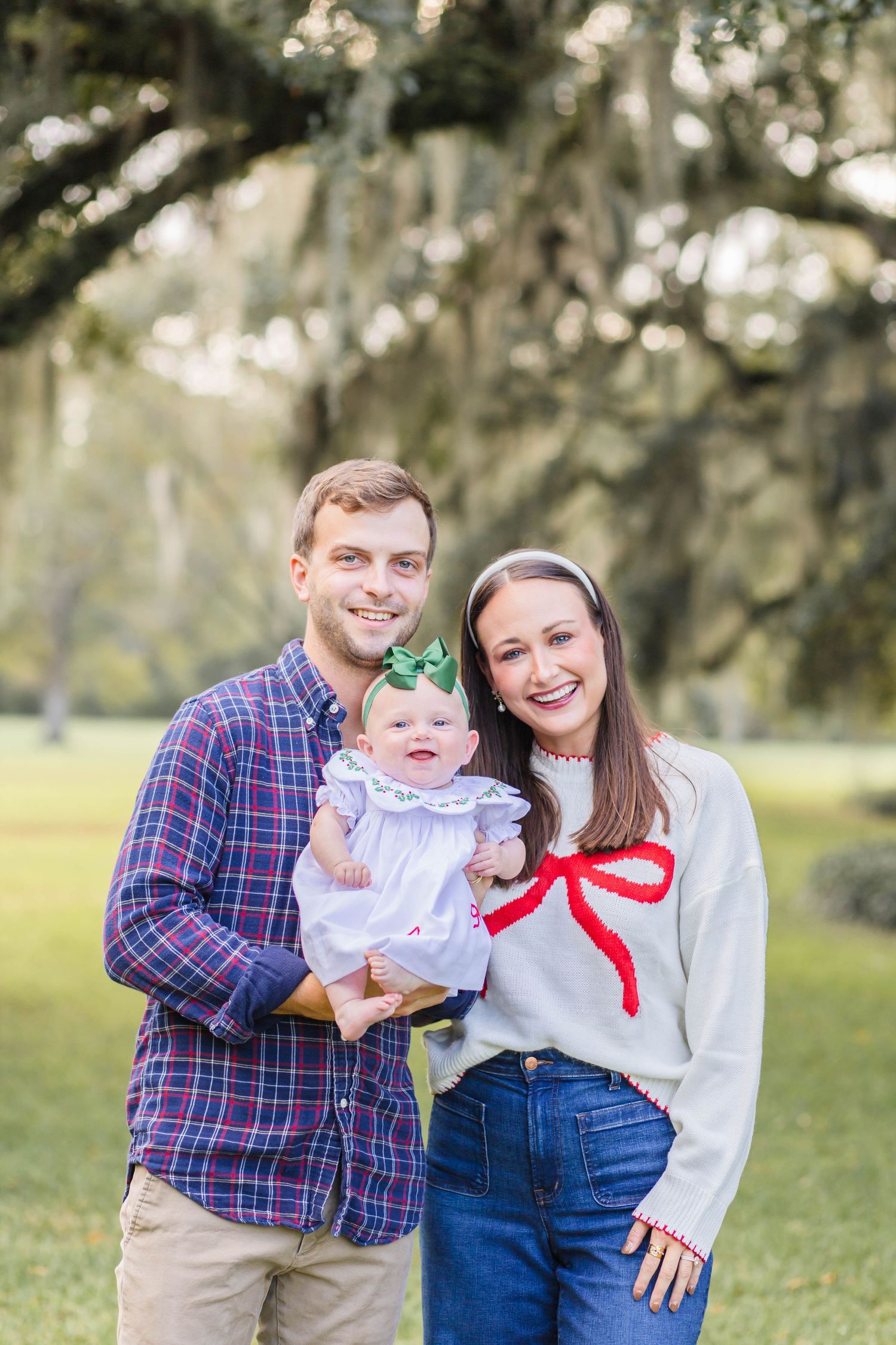 Family portrait outdoors with Spanish moss trees in background, wearing casual clothing and standing together.