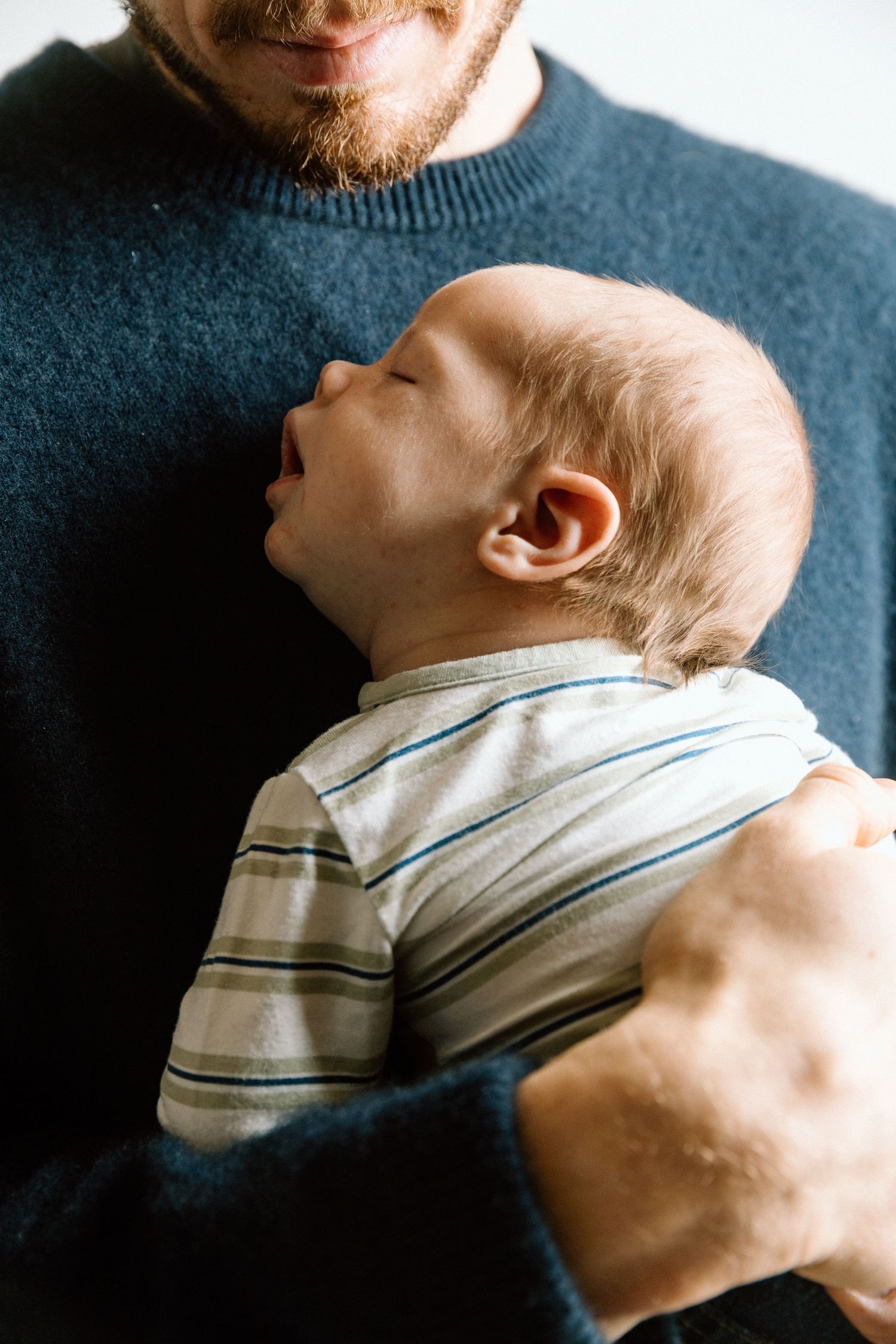 An intimate portrait of a baby in striped clothing resting against a blue sweater.