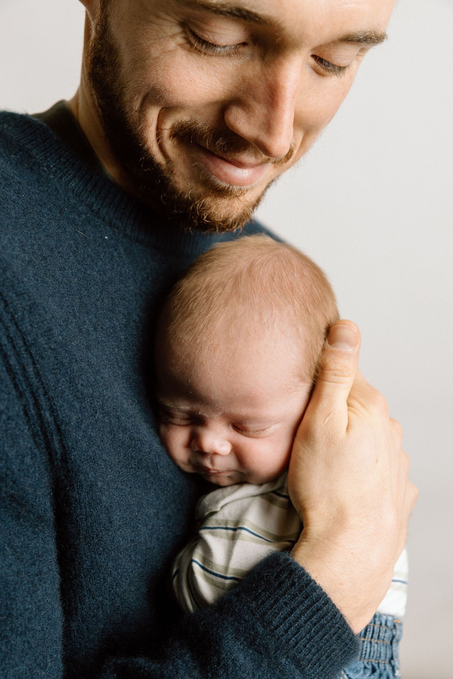 A tender moment between parent and sleeping infant against white background.