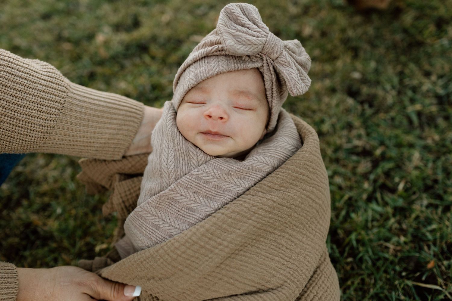 A peaceful sleeping newborn wrapped in beige knit blanket with matching bow headband.