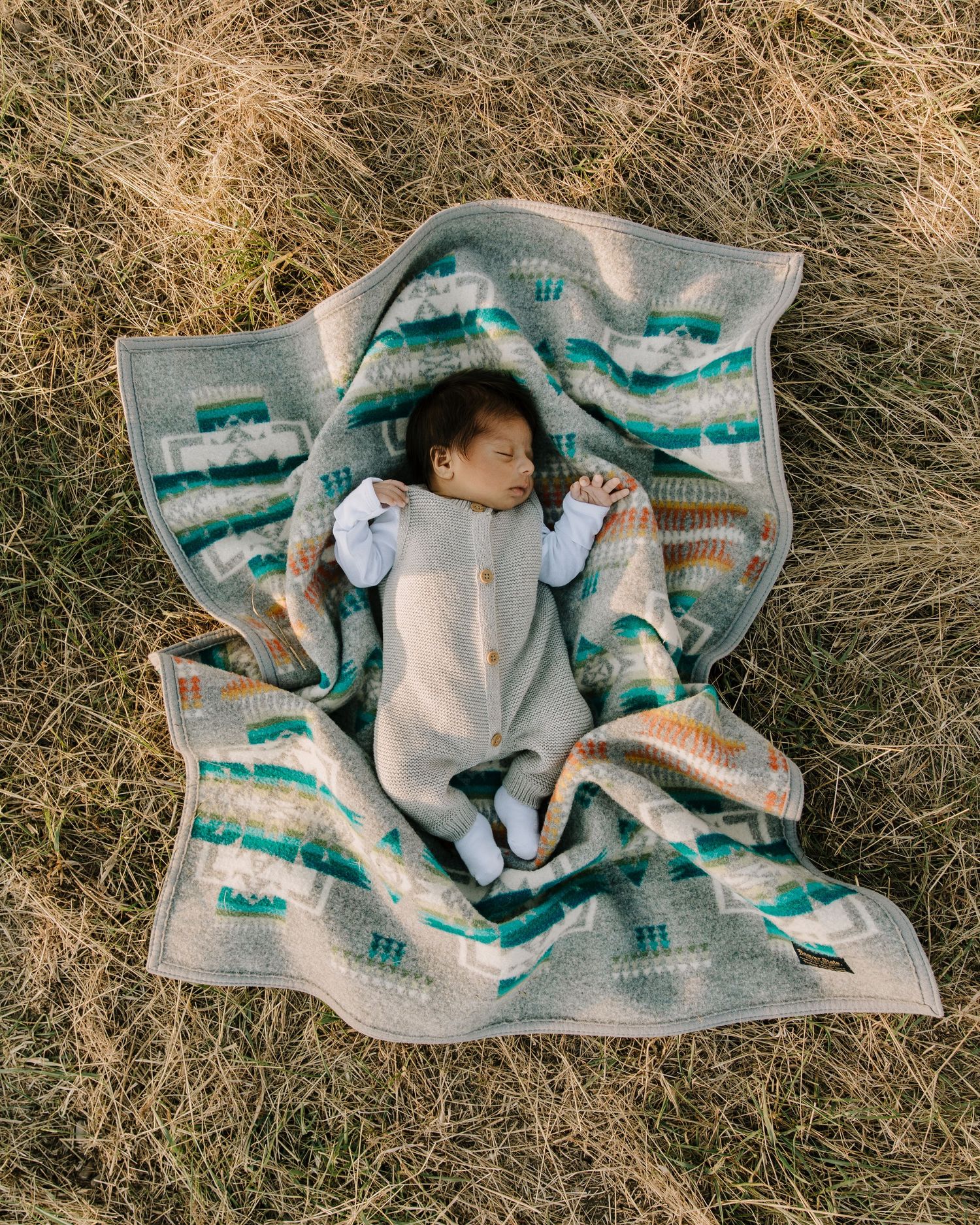 Baby lying on Pendleton blanket in dry grass during golden hour photography session.