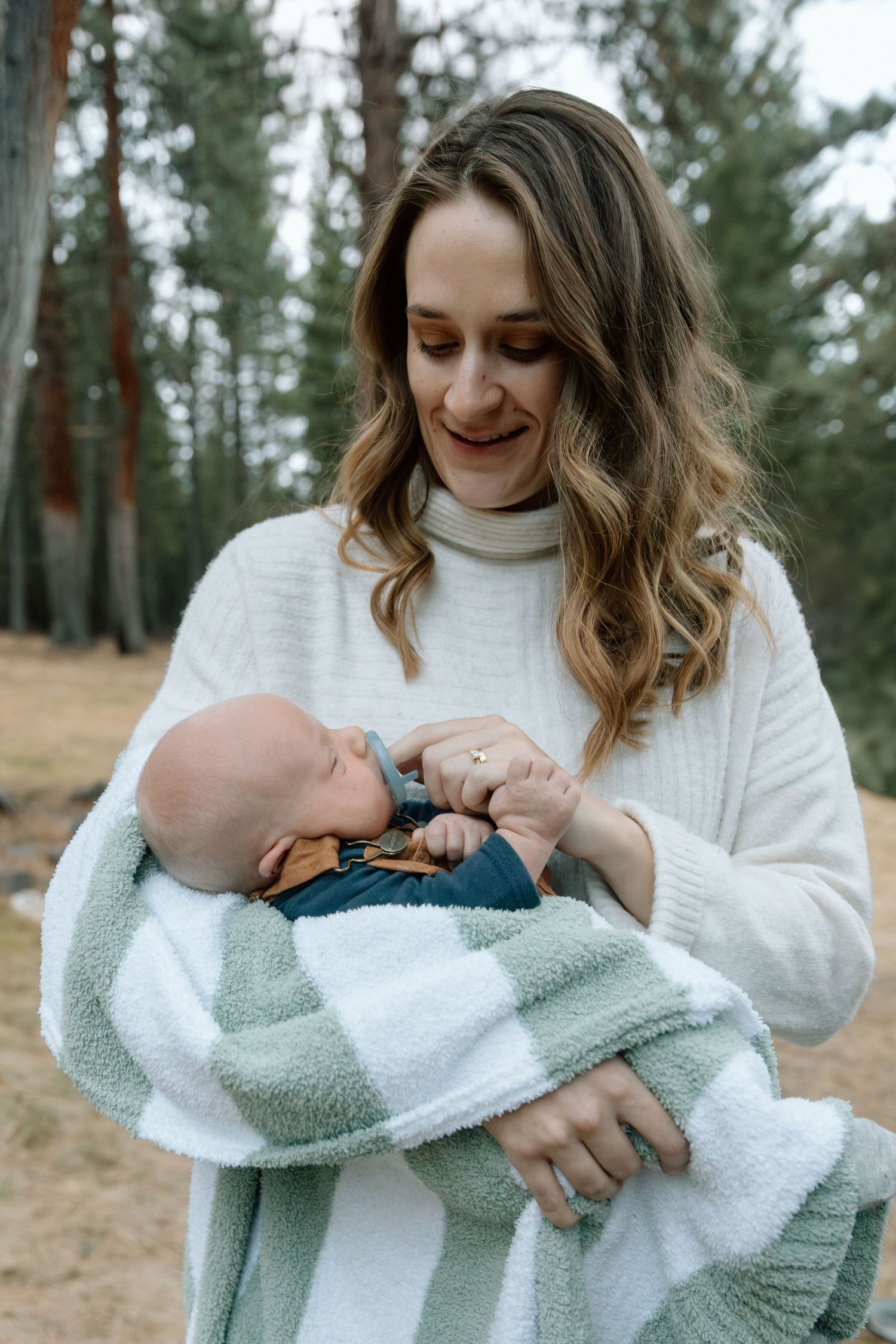 Winter outdoor photography session with white sweater and mint blanket in pine forest.