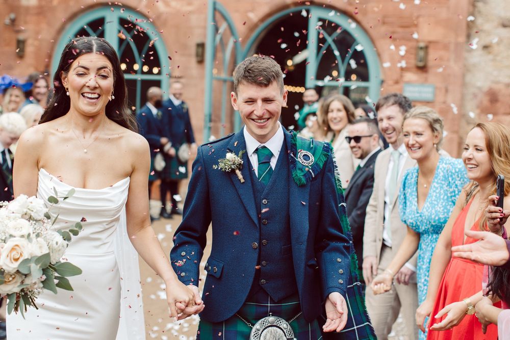 Wedding guests shower newlyweds with confetti during outdoor celebration at brick venue.